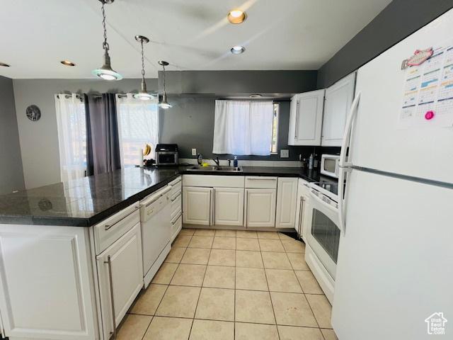 kitchen featuring light tile patterned floors, dark countertops, white appliances, and a peninsula