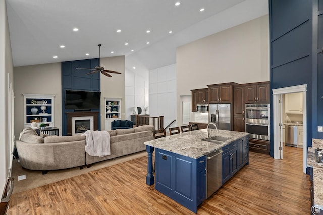 kitchen featuring high vaulted ceiling, ceiling fan, a large fireplace, a sink, and stainless steel appliances