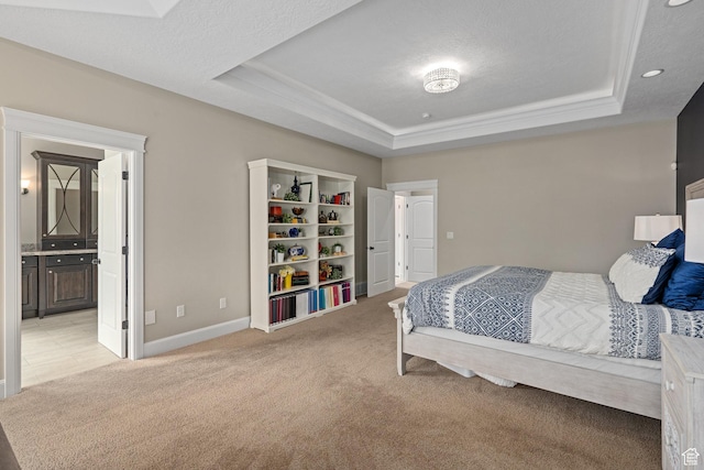 bedroom with light carpet, ensuite bathroom, a tray ceiling, and baseboards