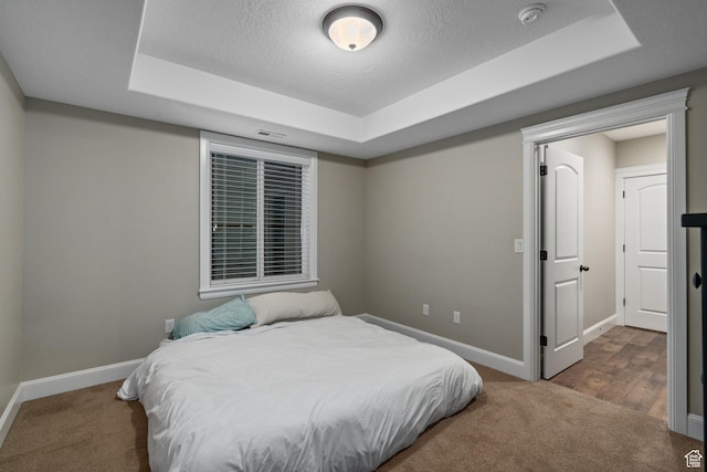 bedroom with a tray ceiling, baseboards, and carpet floors