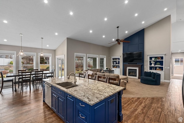 kitchen featuring dishwasher, a sink, a ceiling fan, a center island with sink, and blue cabinets