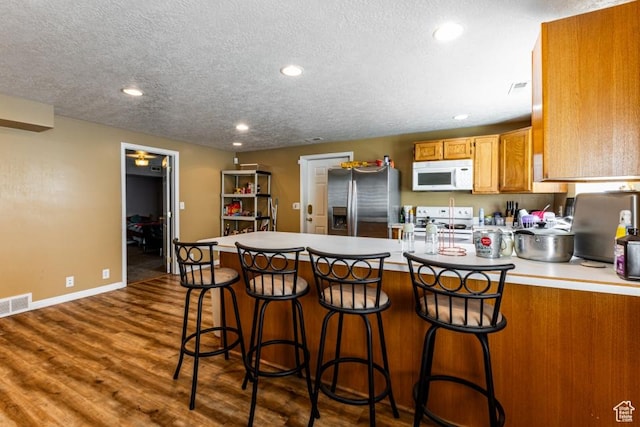 kitchen with dark wood-style floors, light countertops, visible vents, white appliances, and a peninsula