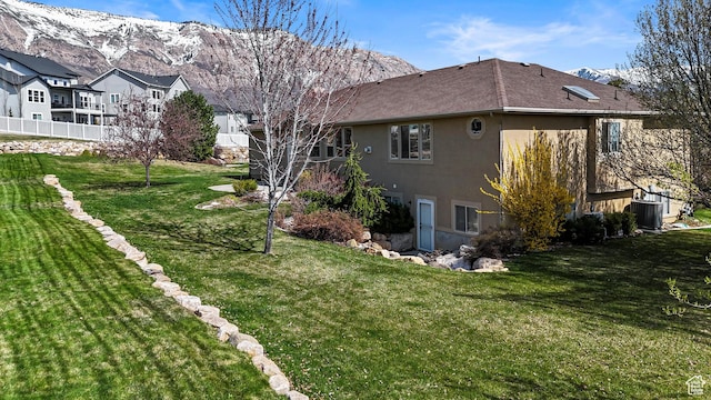 view of property exterior with fence, a mountain view, a yard, cooling unit, and stucco siding