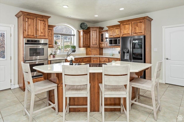 kitchen featuring a sink, recessed lighting, brown cabinets, light countertops, and appliances with stainless steel finishes