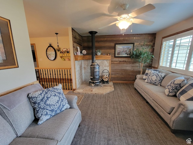 living area featuring a ceiling fan, wood walls, carpet, and a wood stove
