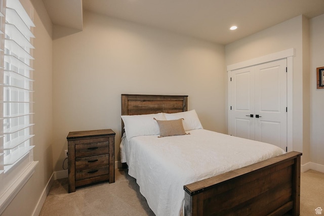 bedroom with a closet, recessed lighting, light colored carpet, and baseboards