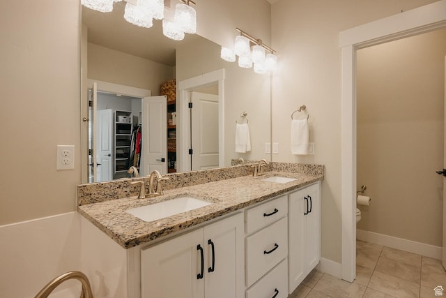full bathroom featuring a walk in closet, double vanity, a sink, and toilet