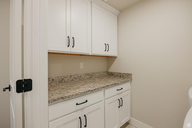 interior space with baseboards, white cabinetry, and light stone countertops