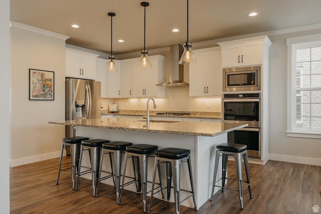 kitchen with wall chimney range hood, dark wood-type flooring, stainless steel appliances, and a sink