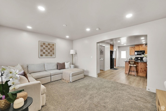 living room with baseboards, recessed lighting, arched walkways, and light colored carpet