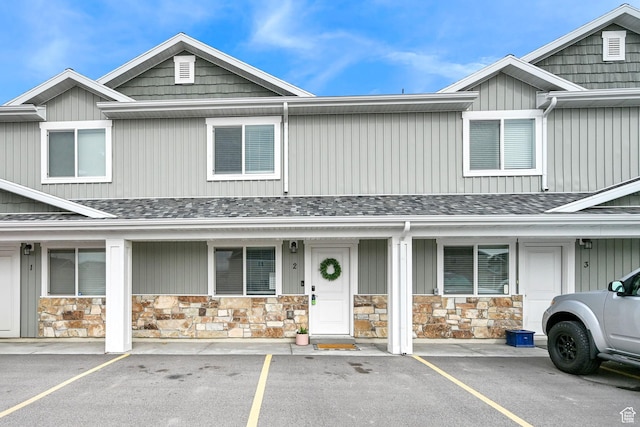 multi unit property with uncovered parking, roof with shingles, covered porch, and stone siding
