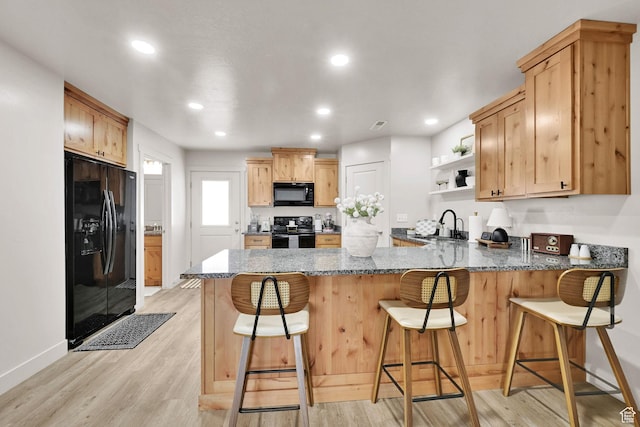 kitchen featuring a peninsula, open shelves, black appliances, dark stone countertops, and light wood finished floors