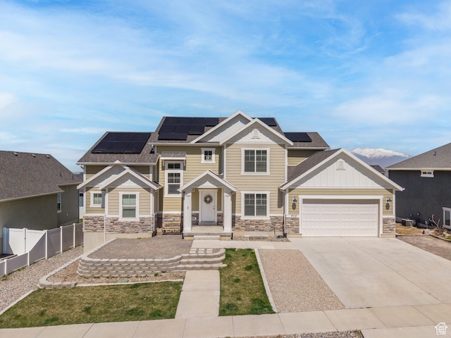 craftsman house with fence, stone siding, solar panels, and concrete driveway