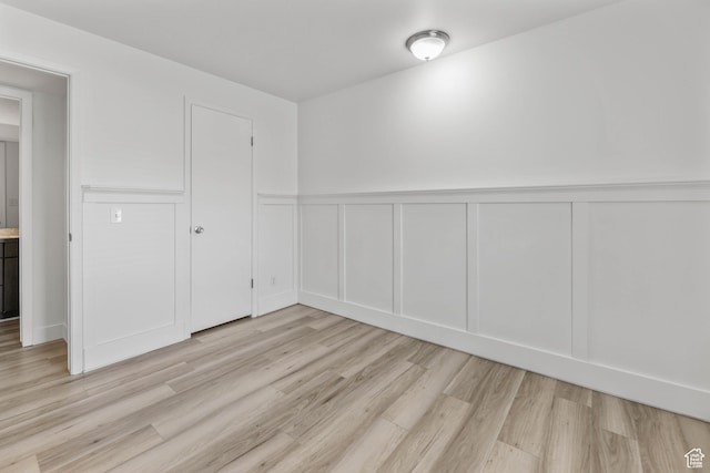 spare room with a decorative wall, light wood-type flooring, and a wainscoted wall