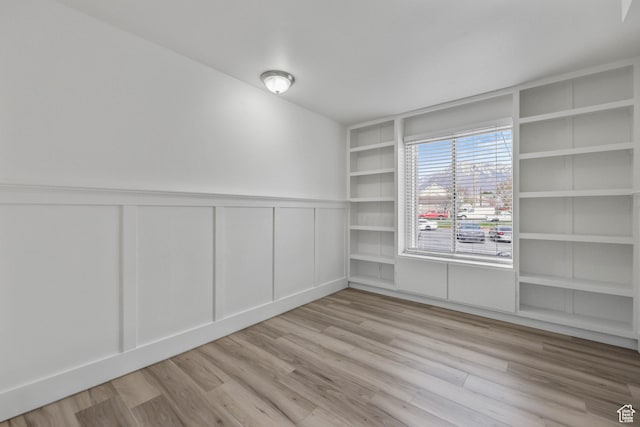 empty room with a decorative wall, wainscoting, built in features, and wood finished floors