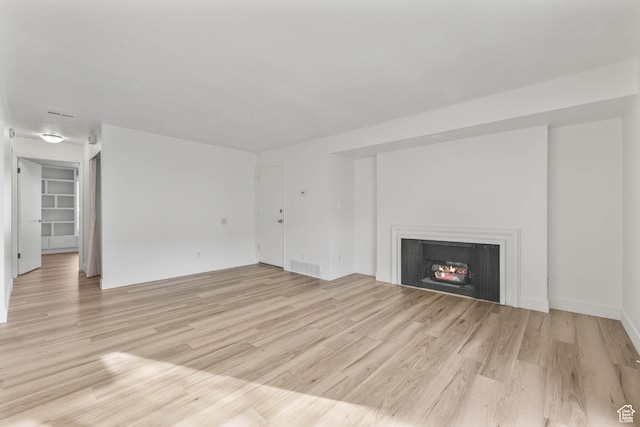 unfurnished living room featuring light wood-style floors, visible vents, a lit fireplace, and baseboards