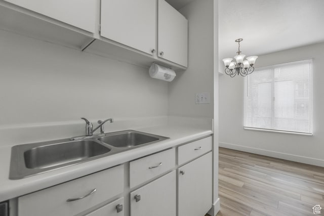 kitchen with white cabinets, a notable chandelier, a sink, light countertops, and light wood-type flooring