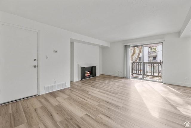 unfurnished living room featuring light wood-style flooring, baseboards, visible vents, and a warm lit fireplace