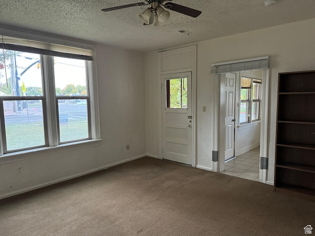 tiled spare room featuring baseboards, a textured ceiling, visible vents, ceiling fan, and carpet