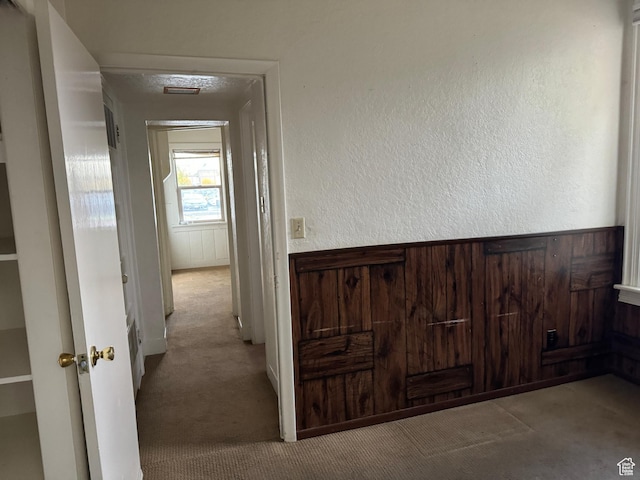 corridor with wooden walls, a textured wall, and carpet