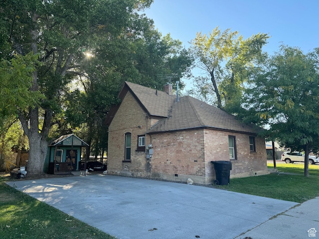 view of home's exterior with a shingled roof, brick siding, crawl space, and a lawn