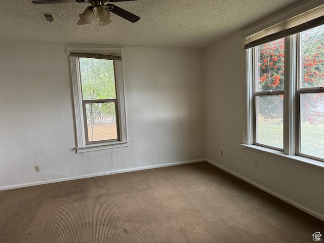 carpeted spare room featuring visible vents, ceiling fan, plenty of natural light, and a textured ceiling
