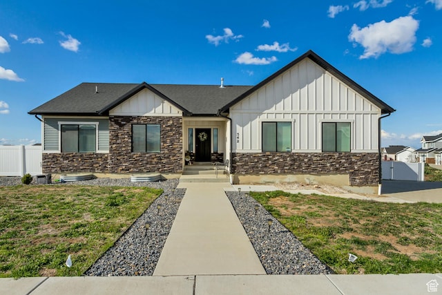 view of front of house featuring board and batten siding, fence, stone siding, and a gate