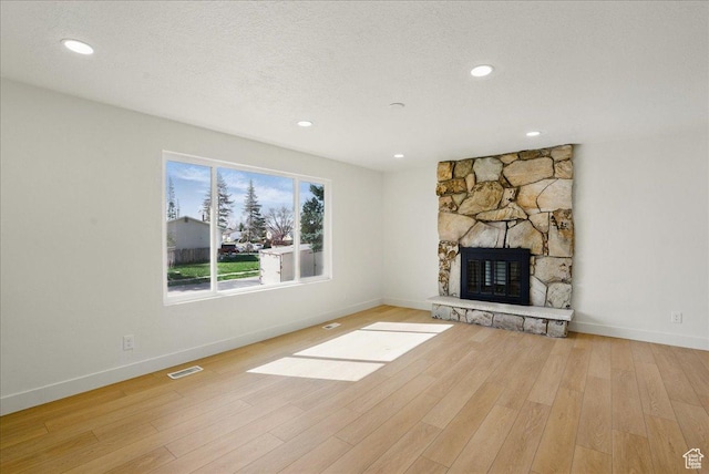 unfurnished living room featuring a stone fireplace, visible vents, baseboards, and wood finished floors