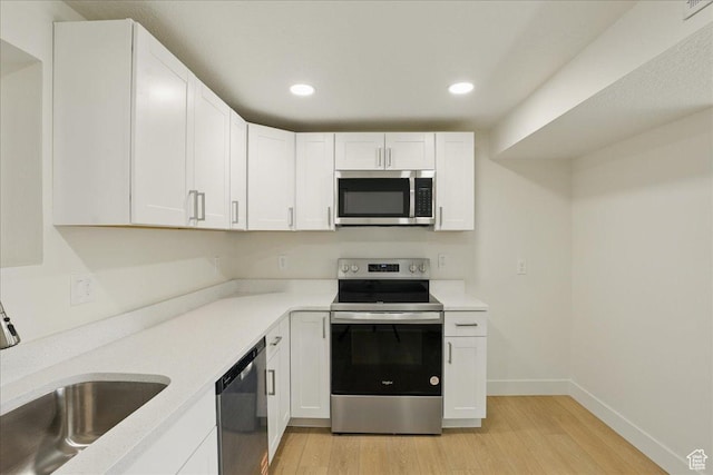 kitchen with light wood-type flooring, white cabinets, light countertops, a sink, and stainless steel appliances
