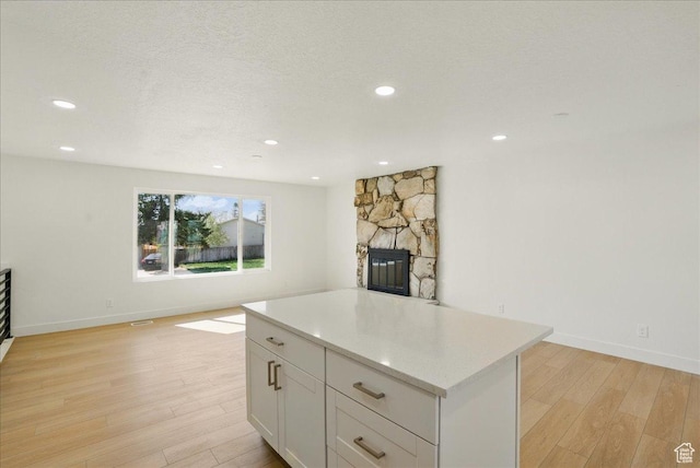 kitchen featuring light wood-type flooring, recessed lighting, a fireplace, light countertops, and white cabinetry