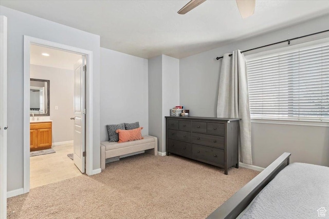 bedroom featuring ensuite bath, light colored carpet, baseboards, and a ceiling fan