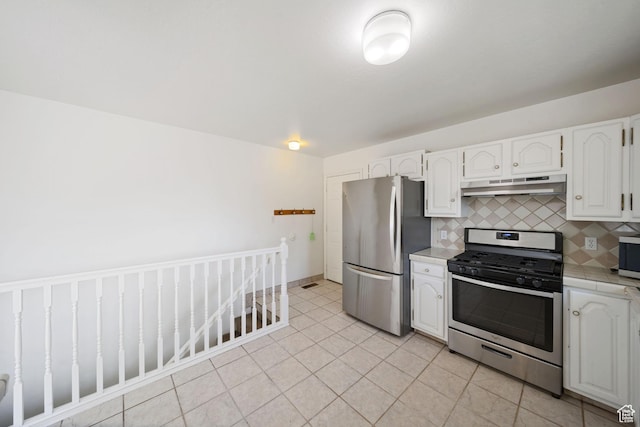 kitchen with tile countertops, white cabinetry, under cabinet range hood, stainless steel appliances, and decorative backsplash