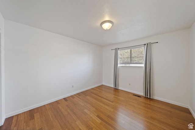 spare room featuring light wood finished floors, visible vents, and baseboards