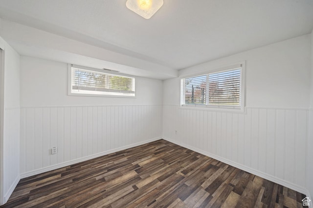 empty room featuring plenty of natural light, dark wood-type flooring, wainscoting, and baseboards