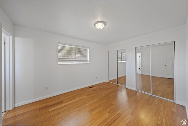 unfurnished bedroom featuring two closets, baseboards, visible vents, and light wood-style floors