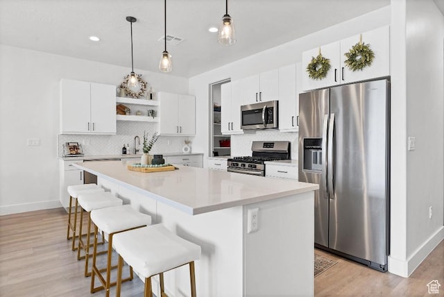 kitchen with baseboards, a breakfast bar, backsplash, open shelves, and appliances with stainless steel finishes