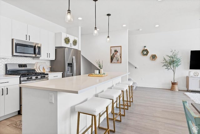 kitchen featuring light wood-style flooring, appliances with stainless steel finishes, a breakfast bar area, and backsplash