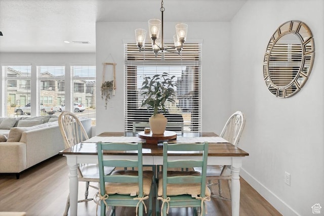 dining room featuring a notable chandelier, baseboards, visible vents, and wood finished floors