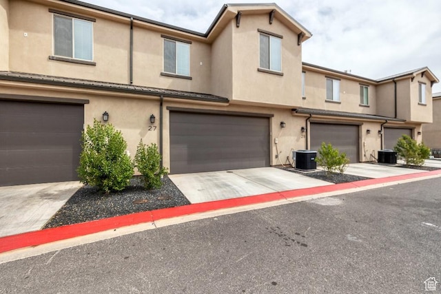 view of property with an attached garage, driveway, stucco siding, and central AC