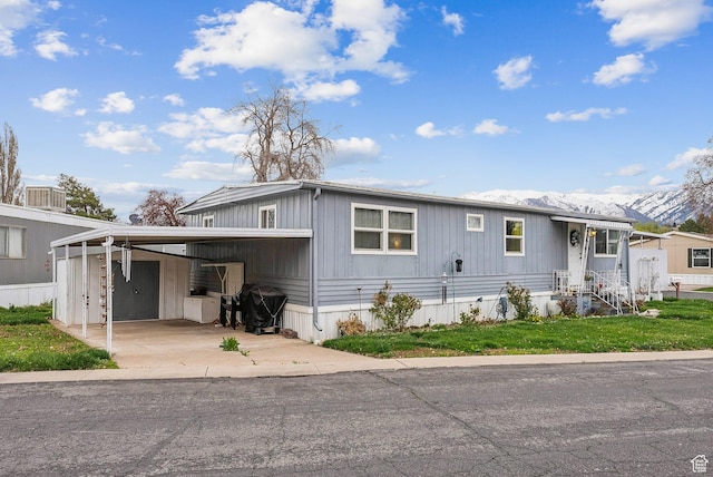 5100 S 1050 W Unit H138, Riverdale, UT 84405 - manufactured / mobile home with concrete driveway, a mountain view, a front lawn, an attached carport, and central AC unit
