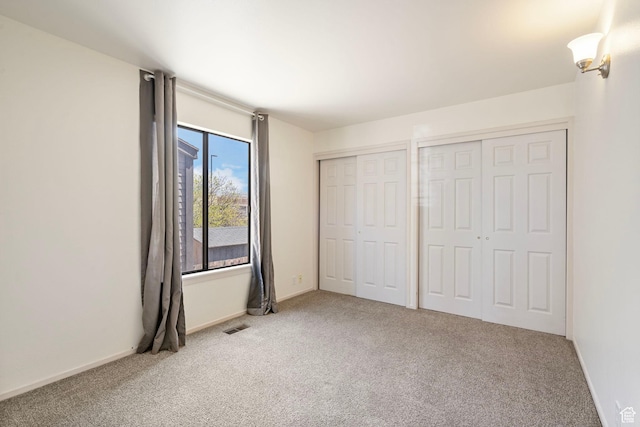 unfurnished bedroom with baseboards, carpet, two closets, and visible vents