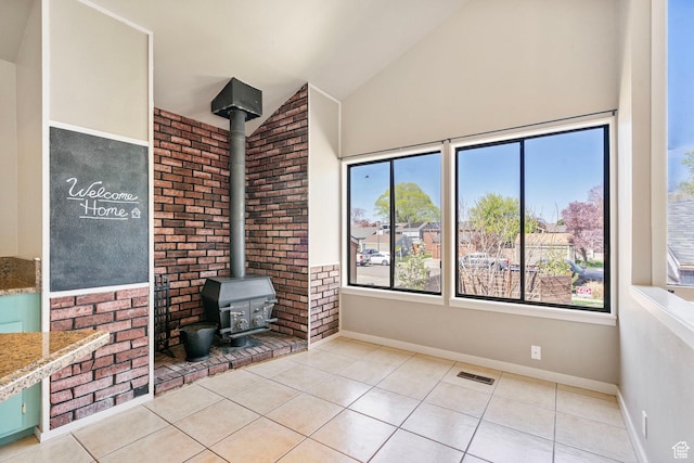 interior space with baseboards, a wood stove, visible vents, and high vaulted ceiling