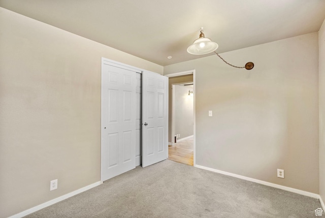 unfurnished bedroom featuring baseboards, a closet, and light colored carpet
