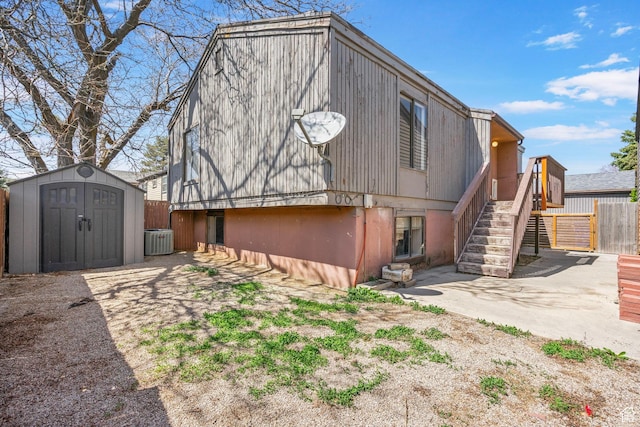 back of house featuring fence, a shed, stairway, an outbuilding, and central air condition unit