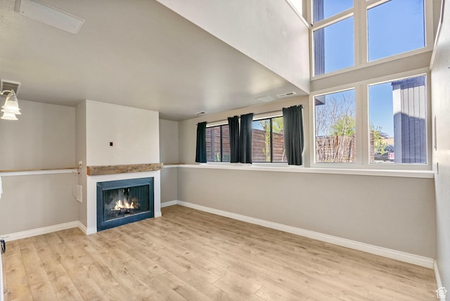 unfurnished living room with baseboards, wood finished floors, and a lit fireplace