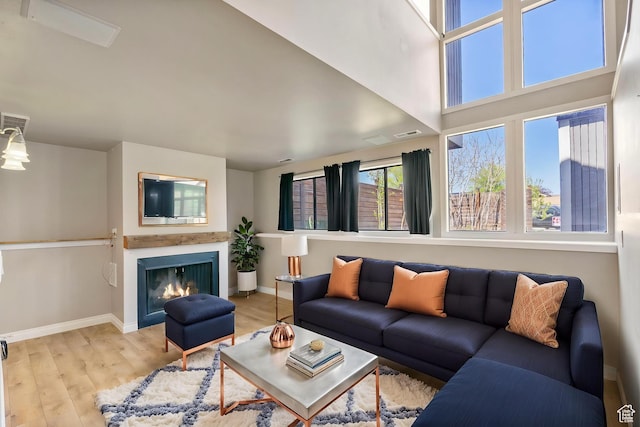 living area featuring baseboards, wood finished floors, and a lit fireplace