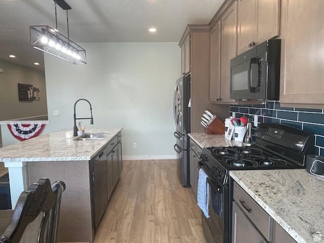 kitchen featuring tasteful backsplash, a sink, black appliances, light wood finished floors, and a center island with sink