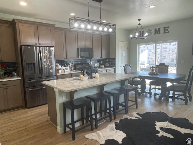 kitchen with stainless steel refrigerator with ice dispenser, a sink, a chandelier, black microwave, and decorative backsplash