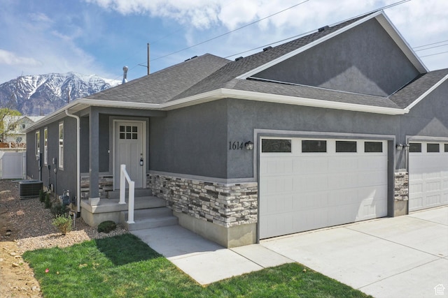 view of front facade with a garage, stucco siding, stone siding, a mountain view, and driveway