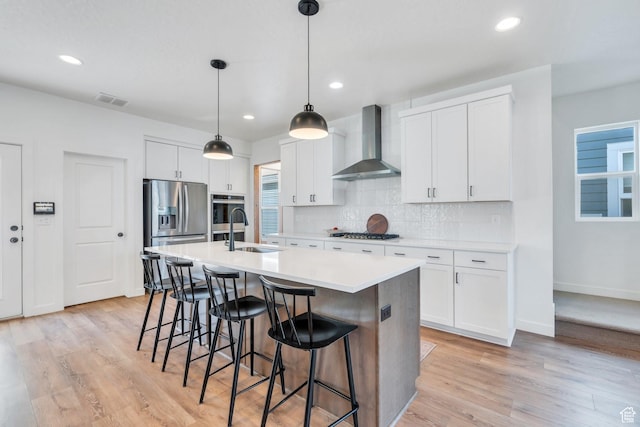 kitchen featuring an island with sink, wall chimney range hood, gas cooktop, a sink, and stainless steel fridge